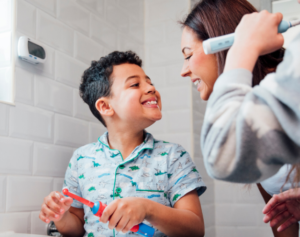 little boy brushing teeth smiling at mom