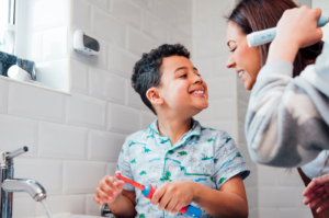 little boy brushing teeth smiling at mom