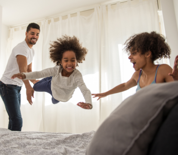 little girl jumping on bed with parents