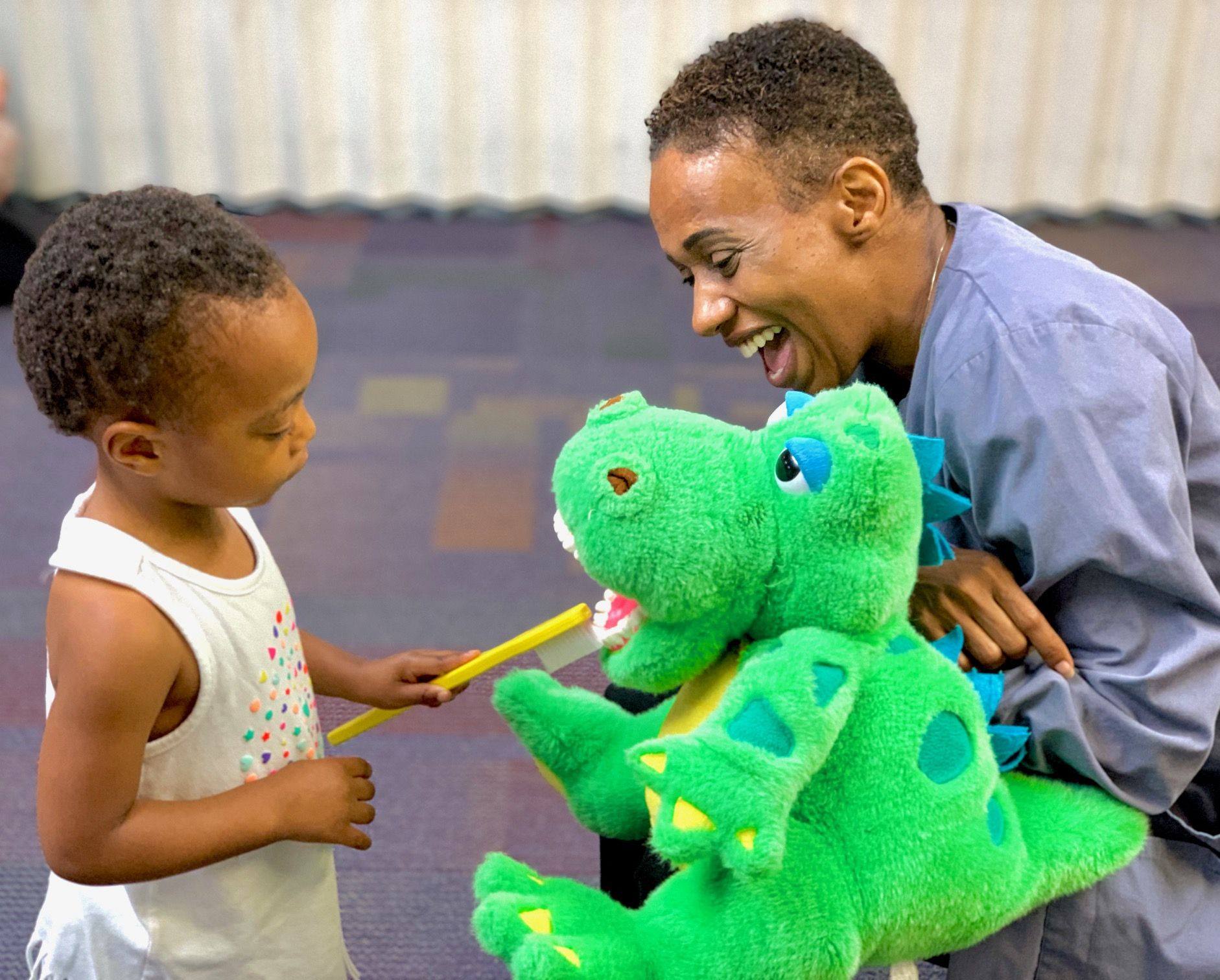 little kid brushing puppets teeth with staff member